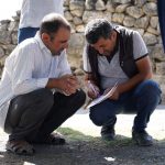 Engineers compare survey records beside a rail embankment